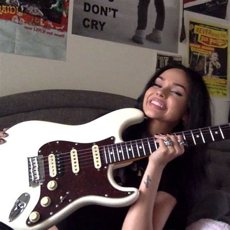 A Woman Sitting On Top Of A Couch Holding An Electric Guitar In Front Of Her Face