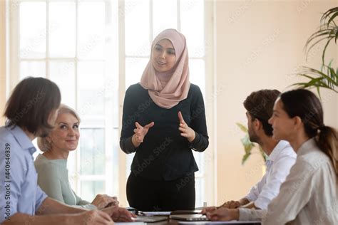 smiling asian muslim team leader talking to diverse employees at briefing businesswoman wearing