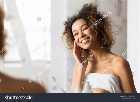 Happy African American Girl Touching Face With Perfect Smooth Skin Looking In Mirror In Bathroom
