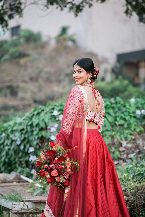 A Woman In A Red And Gold Lehenga With Flowers On Her Head Holding A