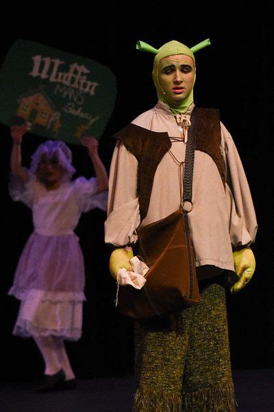 Two People Dressed In Costumes On Stage With One Holding Up A Sign That