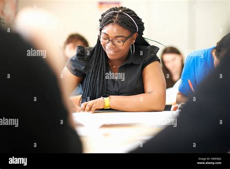 Teenage Female Student Writing At Desk In College Classroom Stock Photo