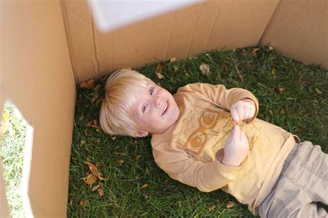 Young Child Laying In Grass While Playing In Cardboard Box Fort Stock