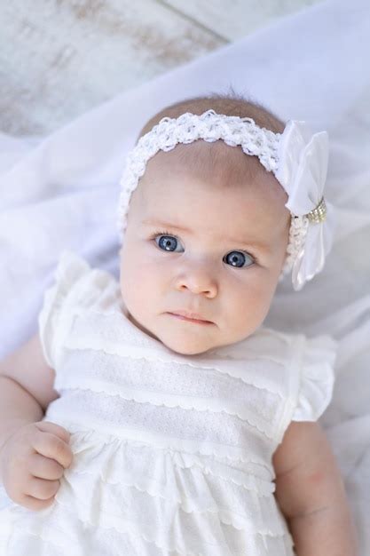 카메라를 보고 흰색 배경에 그녀의 등에 누워 흰 옷에 파란 눈을 가진 귀여운 아기 소녀 프리미엄 사진