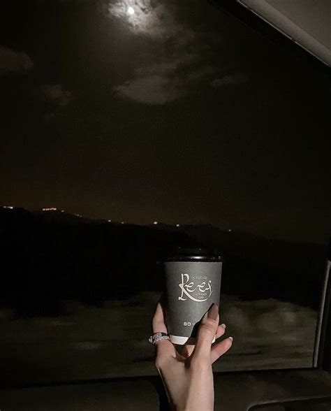 A Person Holding Up A Coffee Cup In Front Of A Window With The Moon