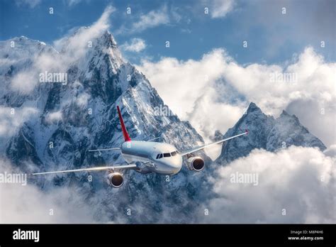 Airplane Is Flying Over Low Clouds Against Mountains With Snowy Peaks