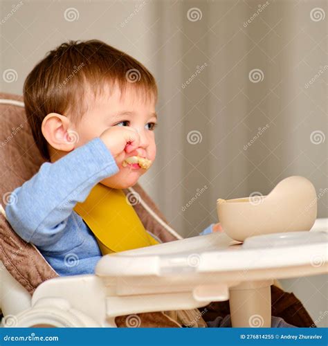 Toddler Baby Eats Porridge With A Spoon While Sitting At The Table On A