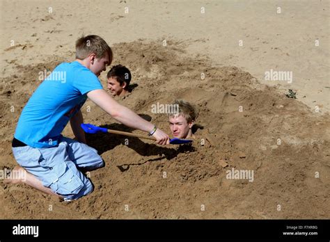 A Boy Buries Two Others Up To Their Necks In The Sand Stock Photo Alamy