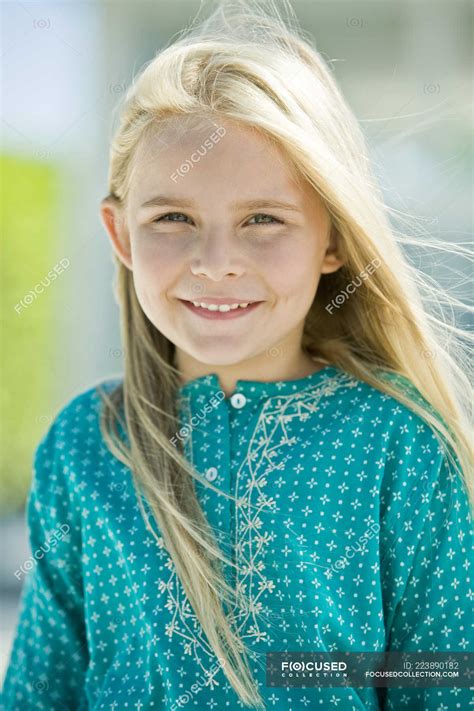 Portrait Of Smiling Little Blonde Girl Looking At Camera On Blurred