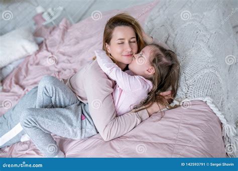 Beautiful Young Mother And Her Little Daughter Are Lying Together On The Bed In The Bedroom