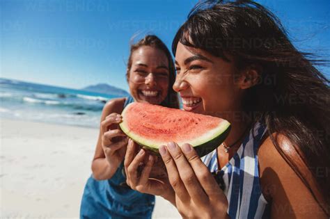 Two Young Women Holding Slice Of Watermelon And Smiling On The Beach
