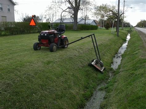 A Lawn Mower Sitting On The Side Of A Road Next To A Small Ditch