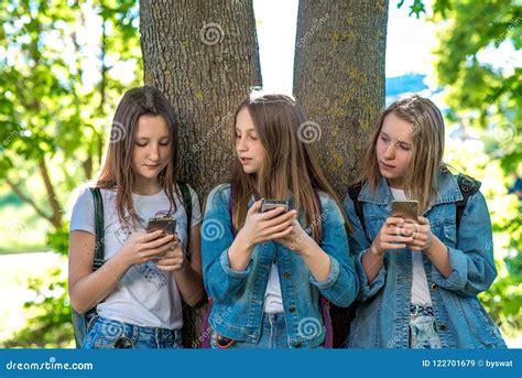 Three Girls Schoolgirl Teen In Summer Park By Tree He Holds A Smartphone In His Hands Writes