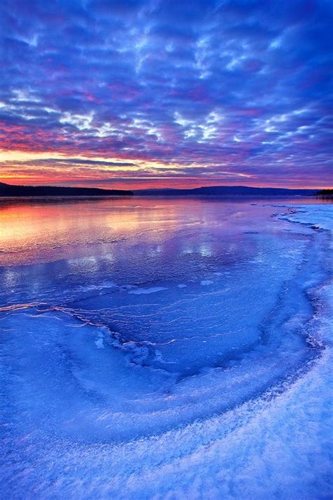 The Sun Is Setting Over An Icy Lake With Blue Water And White Foam On It