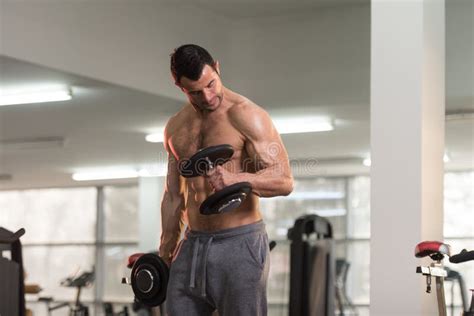 Hombre Muscular Que Ejercita El Bíceps Con Pesa De Gimnasia Foto de