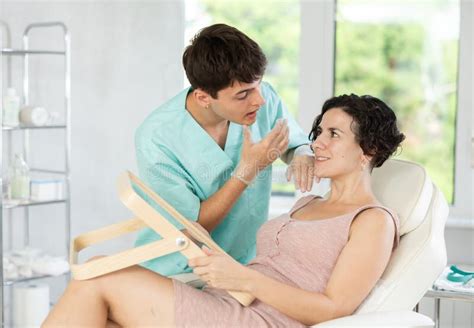 Male Beautician Giving Consultation To Woman Patient With Mirror In