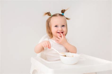 Premium Photo Baby Girl Sitting In A High Chair Eating Porridge