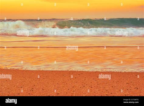 Landscape Of A Beach Surrounded By Sea Waves During An Orange Sunset In