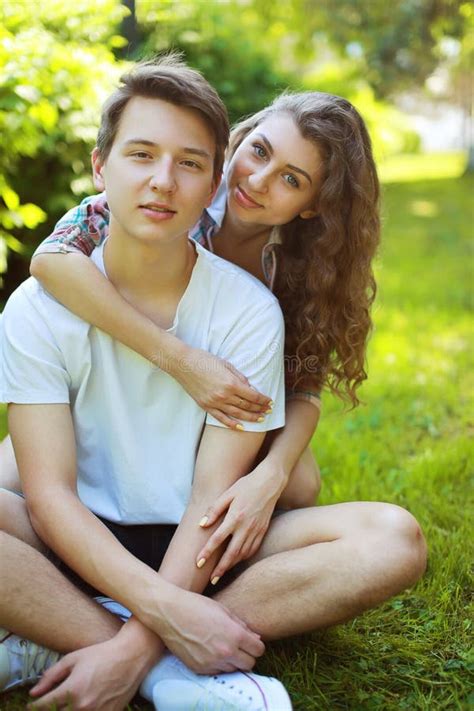 Portrait Happy Couple Teenagers Sitting On The Grass In Summer Stock