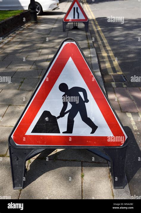 Triangular Roadworks Sign On Pavement With Road Narrows On Right Sign