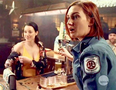 Two Women In Police Uniforms Sitting At A Bar And One Woman Is Holding