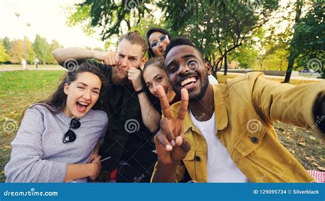 Multiracial Group Of Friends Is Taking Selfie In Park Sitting On Blanket Posing And Looking At