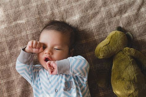 Cute Baby Boy Yawning Lying On Blanket With Stuffed Animal By