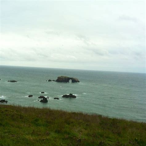 An Ocean View With Rocks In The Foreground And Green Grass On The Other