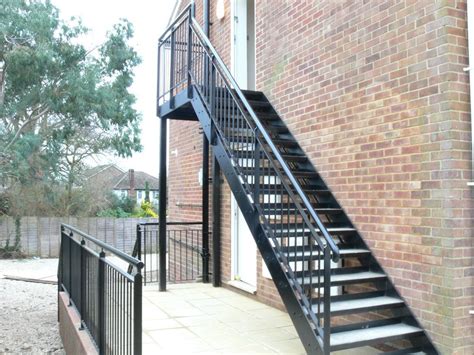 A Black Stair Case Next To A Brick Building With A Metal Hand Rail And