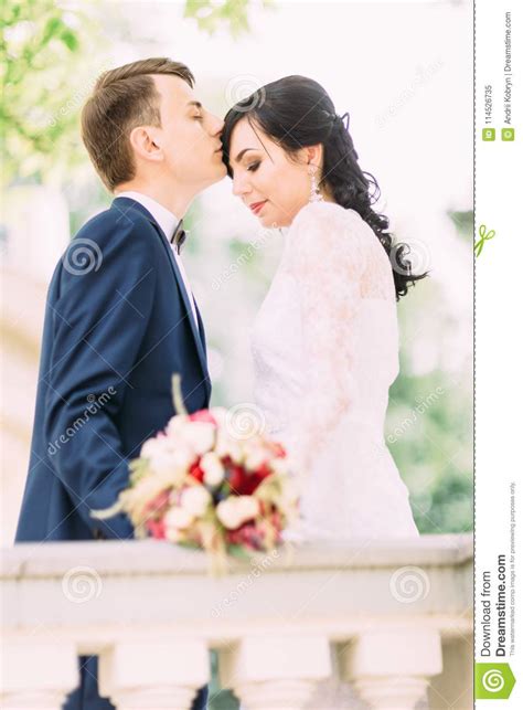 The Groom Is Kissing The Bride In The Forehead Half Length Portrait