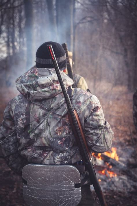 Hunter With Gun At Campfire In Forest During Hunting Season View From