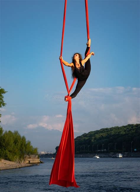 beautiful and flexible female circus artist dancing with aerial silk with sky and river
