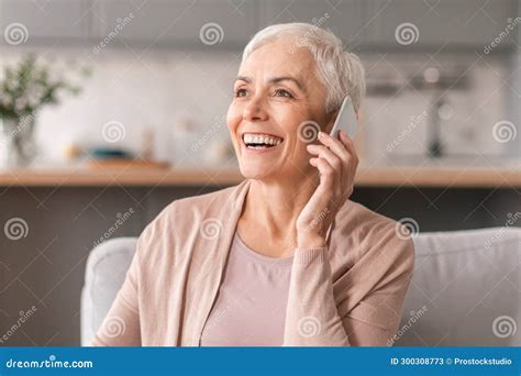 Smiling Mature Woman Talking On Cellphone Sitting On Sofa Indoor Stock