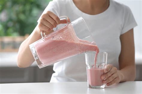 Woman Pouring Strawberry Smoothie From Jug Into Glass Indoors Stock