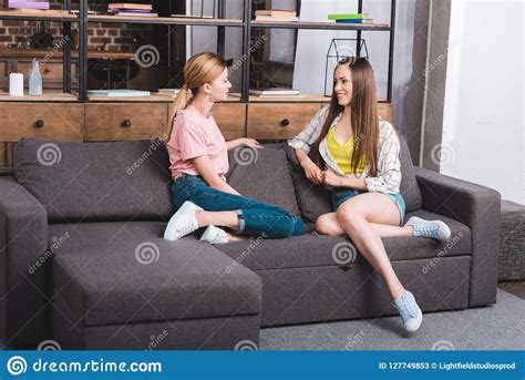 Two Young Female Friends Talking To Each Other While Sitting On Sofa Stock Image Image Of