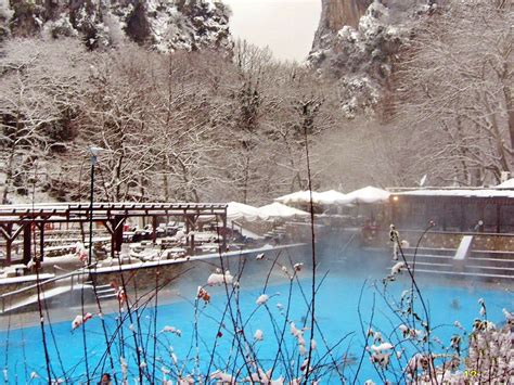 A Blue Pool Surrounded By Snow Covered Trees And Mountains In The