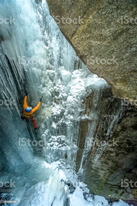 Aerial Perspective Of Ice Climber Ascending Frozen Waterfall In Canyon