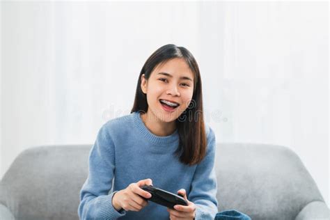 Excited Young Asian Woman Sitting On Sofa And Holding Joystick With