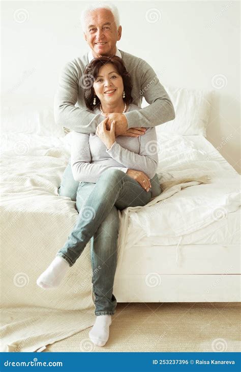 Mature 60 Year Old Couple Hugging While Sitting On The Bed In The Bedroom Love Forever Stock