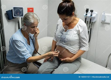 Female Doctor Examining Pregnant Womans Belly With Stethoscope In Examination Room Stock Image