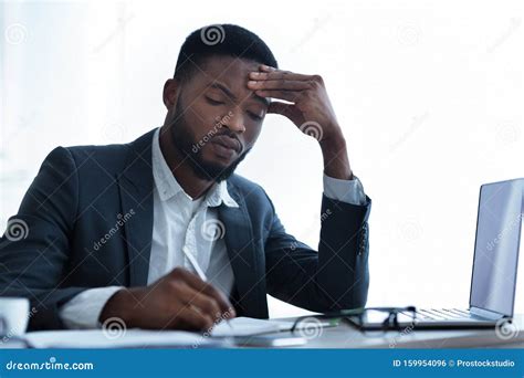 Serious Afro Businessman Filling Paperwork At Workplace In Modern