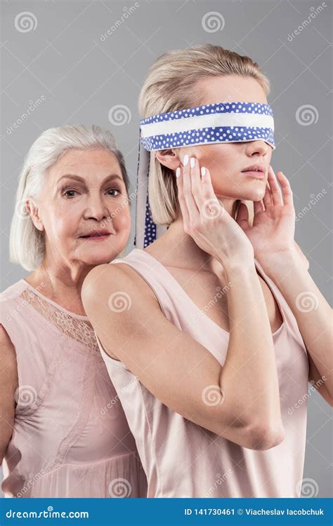 short haired senior mother supporting her blindfolded appealing daughter stock image image of
