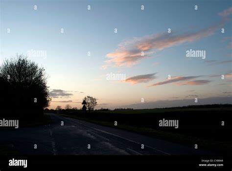 Dark Country Road With Trees And Hedges Silhouetted Against Pale Sky At