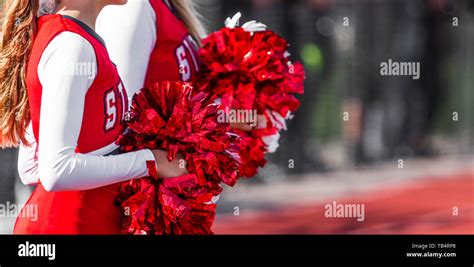 Two High School Cheerleaders With Red And White Pom Poms At A Football Game In Autumn Stock