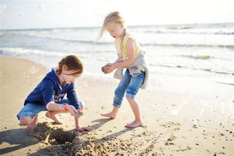 Two Little Sisters Having Fun On A Sandy Beach On Warm And Sunny Summer