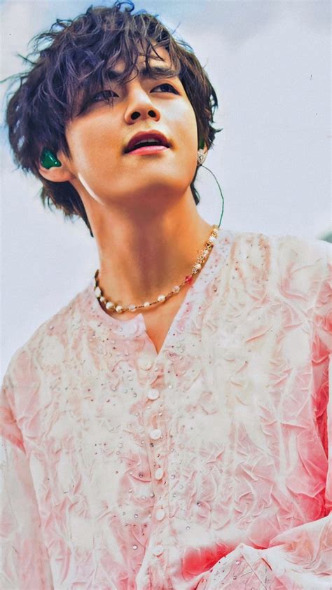 A Young Man With Curly Hair Wearing A Pink Shirt And Gold Necklace