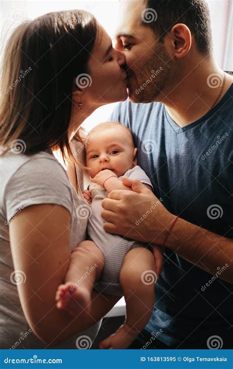 Young Mother And Father Kissing Each Other With Baby On Hands Close Up