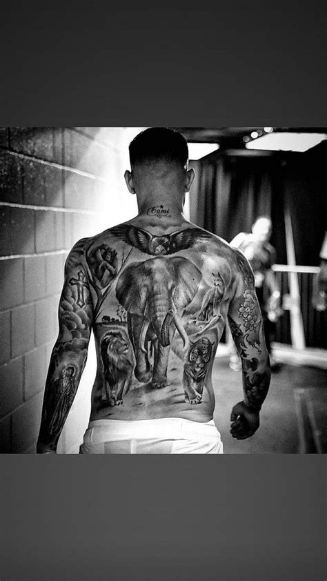 A Man With Tattoos On His Back Walking Down A Hallway Next To A Brick Wall