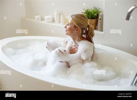 Joyful Young Attractive Woman Sitting In Bath Of Foam And Bubbles And Smiling Taking Bath Stock