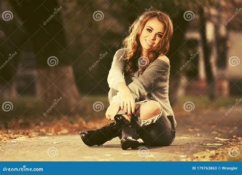 Happy Young Fashion Woman In Ripped Jeans Sitting On Sidewalk Stock